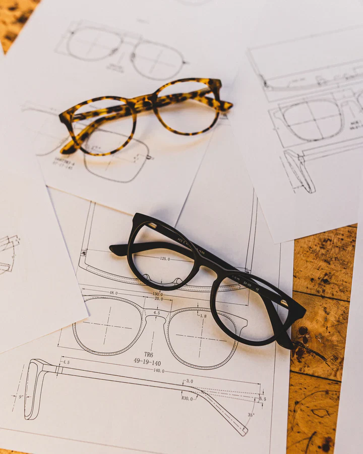 Tortoise and black eyewear prototypes arranged over technical frame sketches